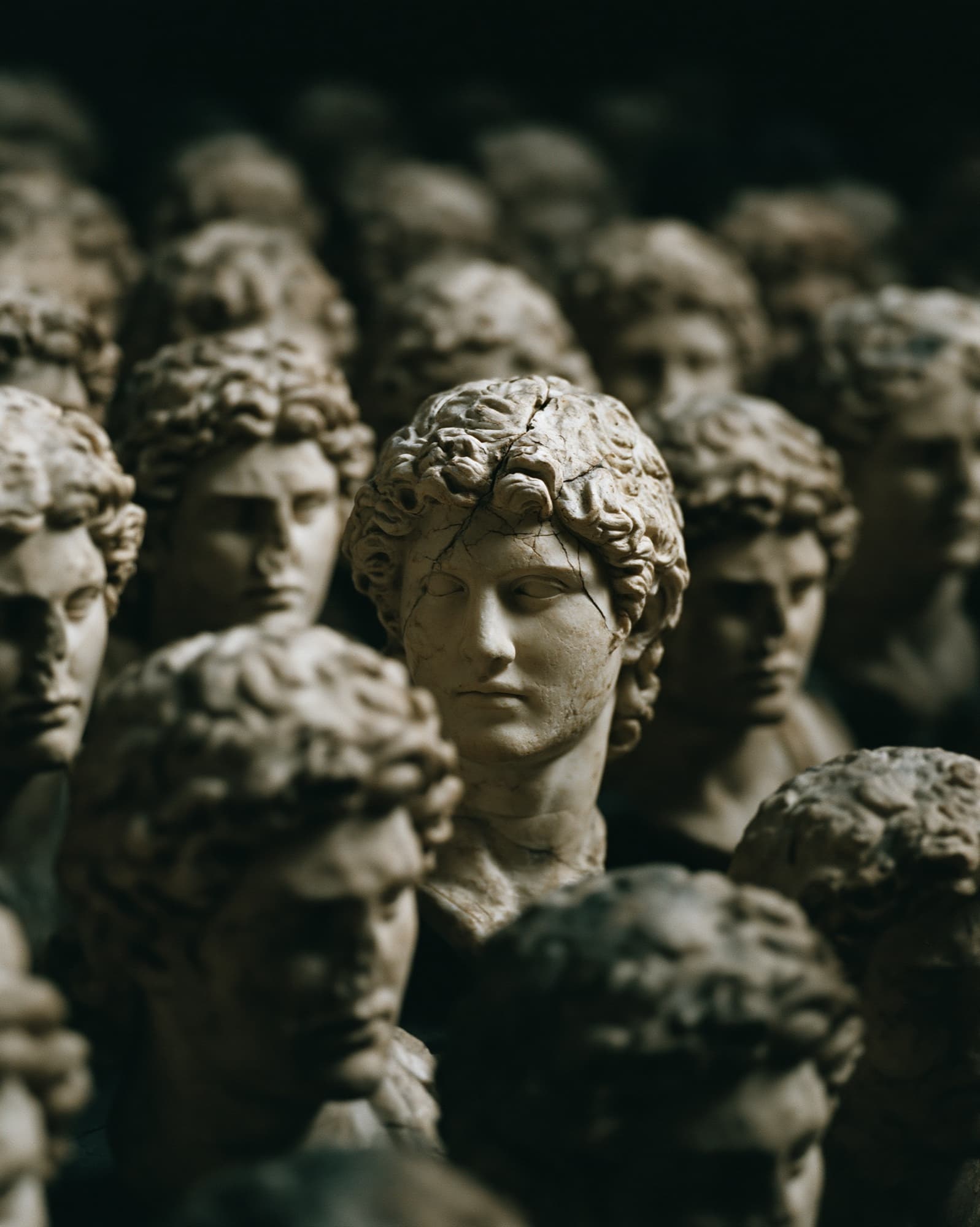 Rows of near-identical classical sculpture heads, one in sharp focus standing apart from the rest